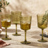Set of green wine glasses on a wooden table with food and plants in the background