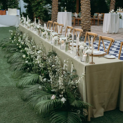 Decorated outdoor wedding table with white flowers and greenery, set against a natural backdrop.