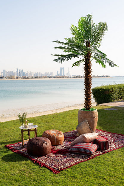 Large artificial palm tree with a sturdy base, set on a lawn near water, ideal for event decor by Party Social.