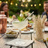 Outdoor setting with a cocktail and snacks on a wooden table, people in the background.