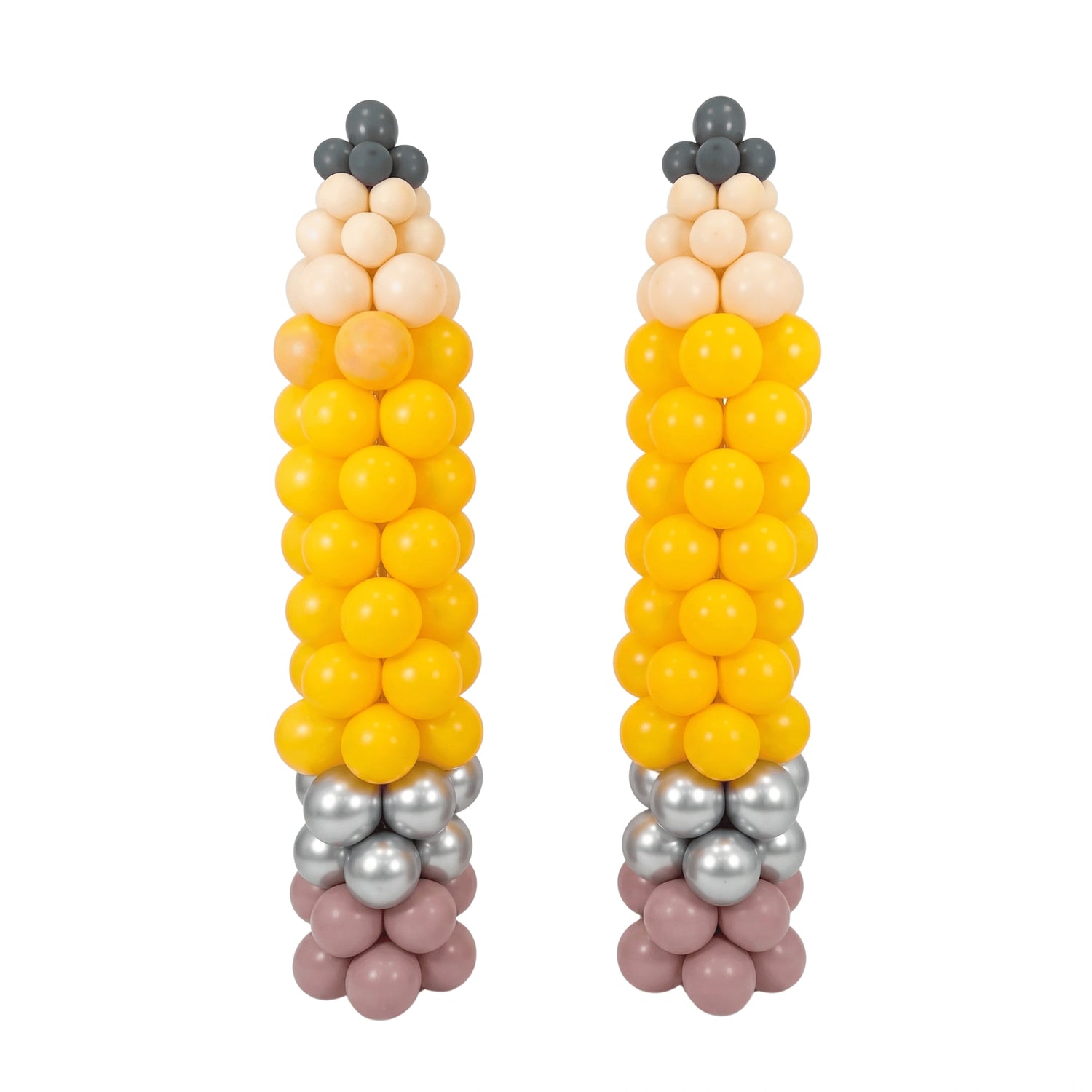 Two balloon sculptures shaped like corn cobs, made from yellow, peach, beige, gray, and dusty pink balloons, set against a plain white background.