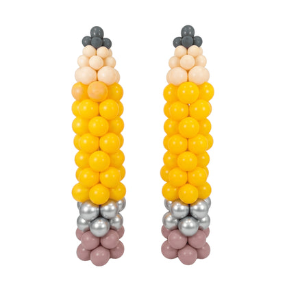 Two balloon sculptures shaped like corn cobs, made from yellow, peach, beige, gray, and dusty pink balloons, set against a plain white background.