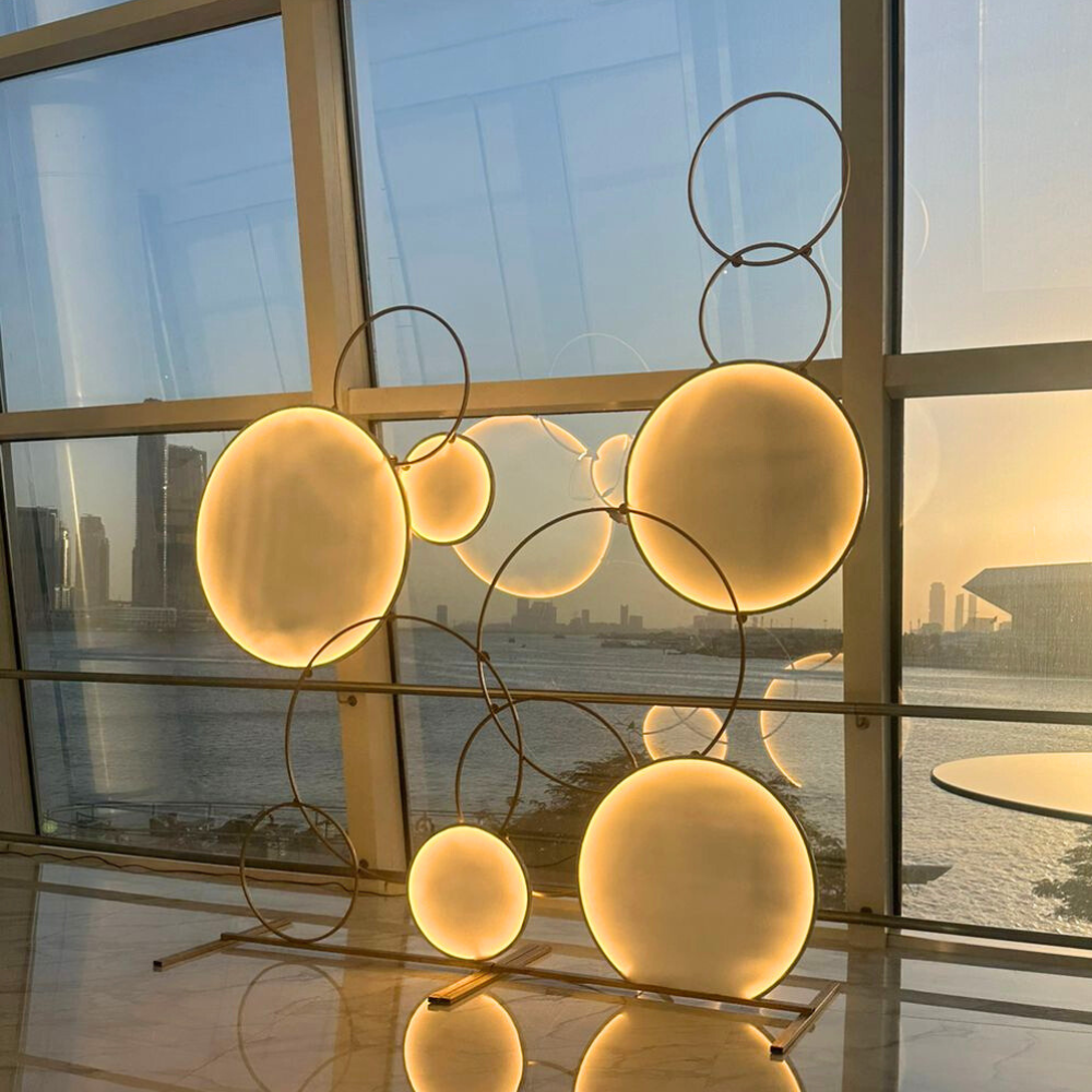CircleScape LED Backdrop: A circular LED sculpture with metal rings, ideal for events like weddings or parties, displayed in front of a window.