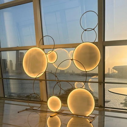 CircleScape LED Backdrop: A circular LED sculpture with metal rings, ideal for events like weddings or parties, displayed in front of a window.