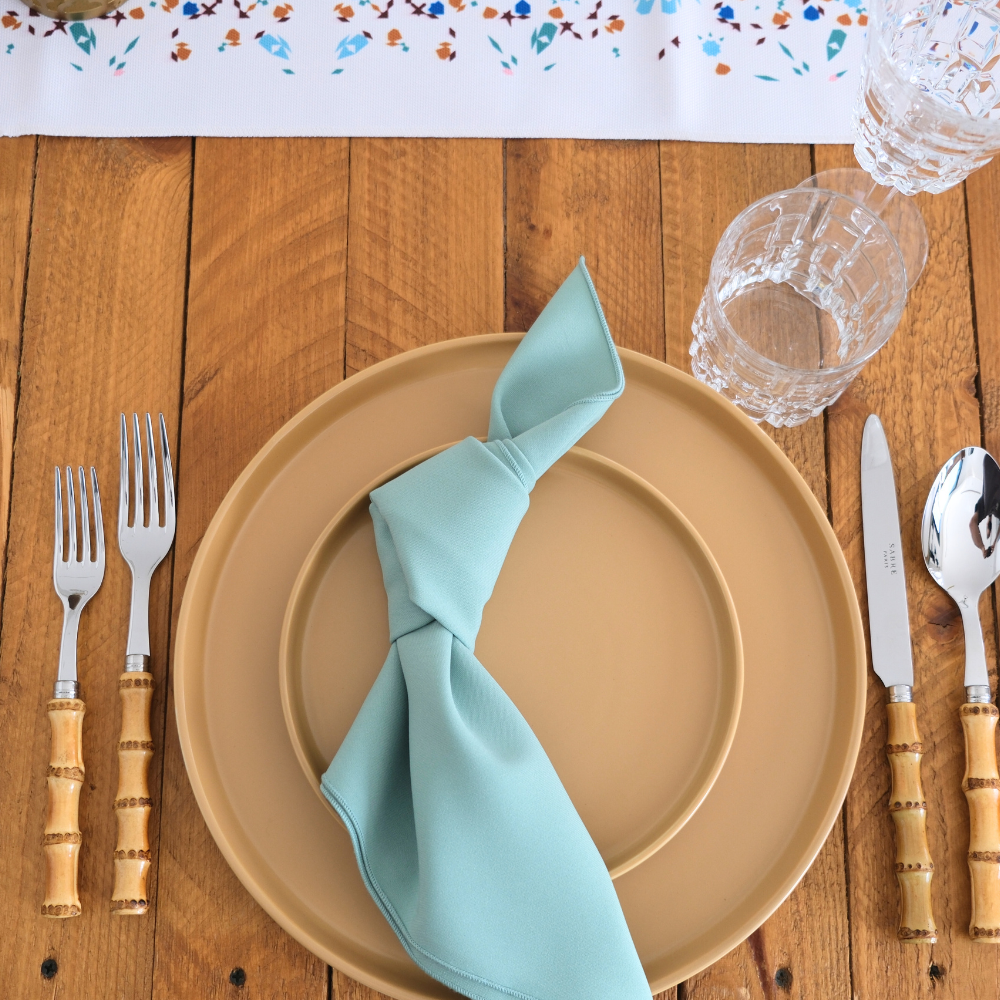 Mustard Ceramic Matte Plates set on a wooden table with bamboo-handle cutlery, teal napkin, and cut-glass tumblers, showcasing modern simplicity for elegant dining.