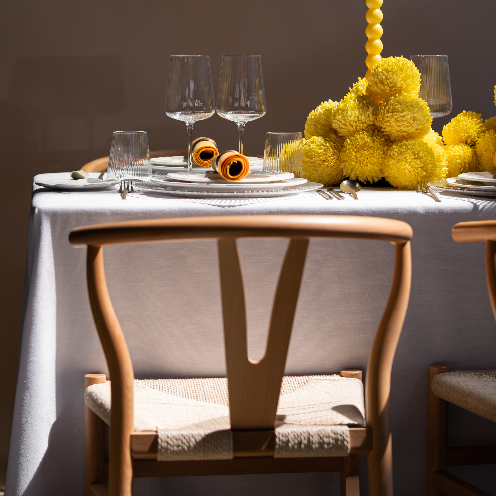 Wishbone Chair with woven seat at elegantly set dining table featuring white plates, yellow-orange napkins, and a yellow floral centerpiece.