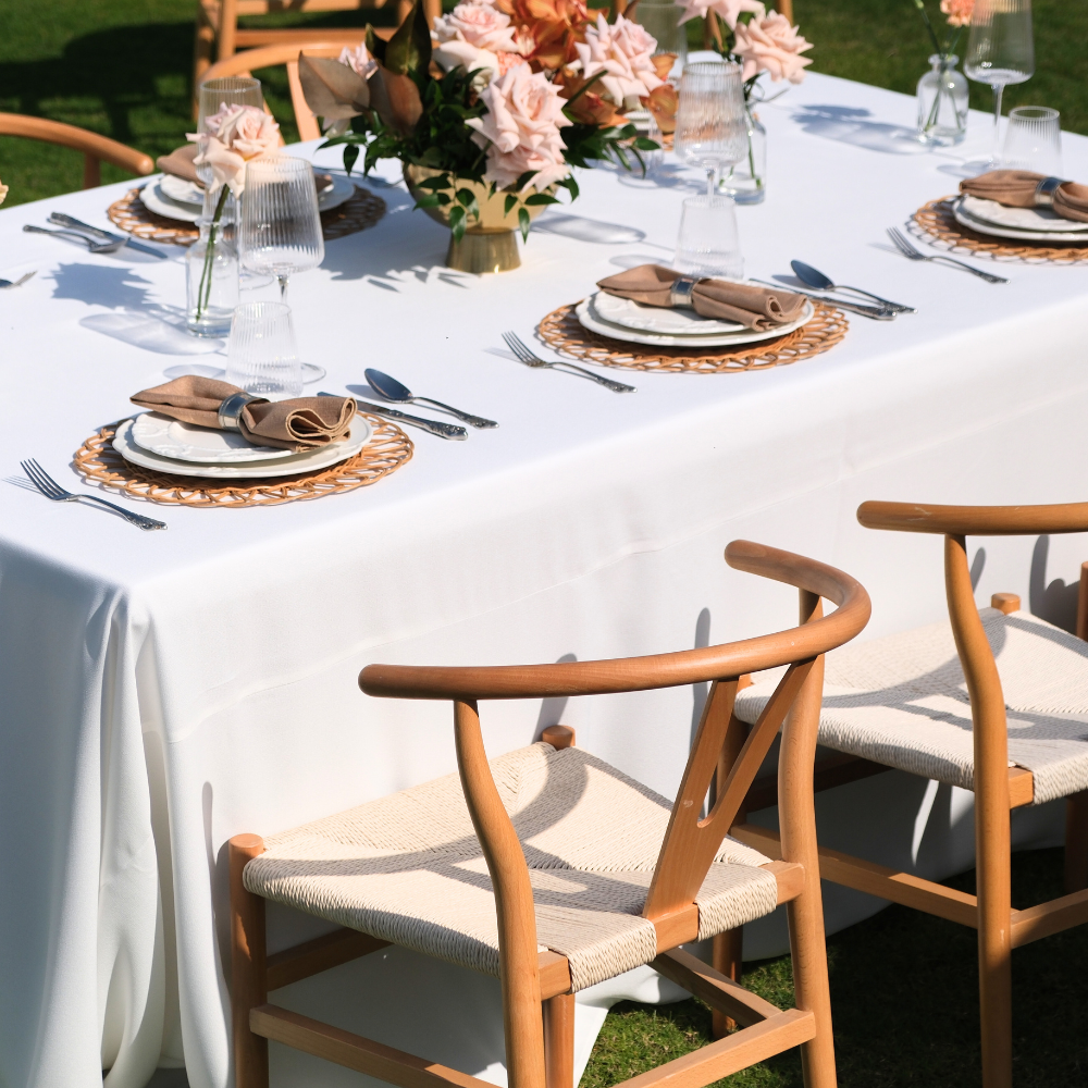 Outdoor dining setup featuring Wishbone Chairs with light wood frames and woven seats around a table, highlighting minimalist elegance for events.