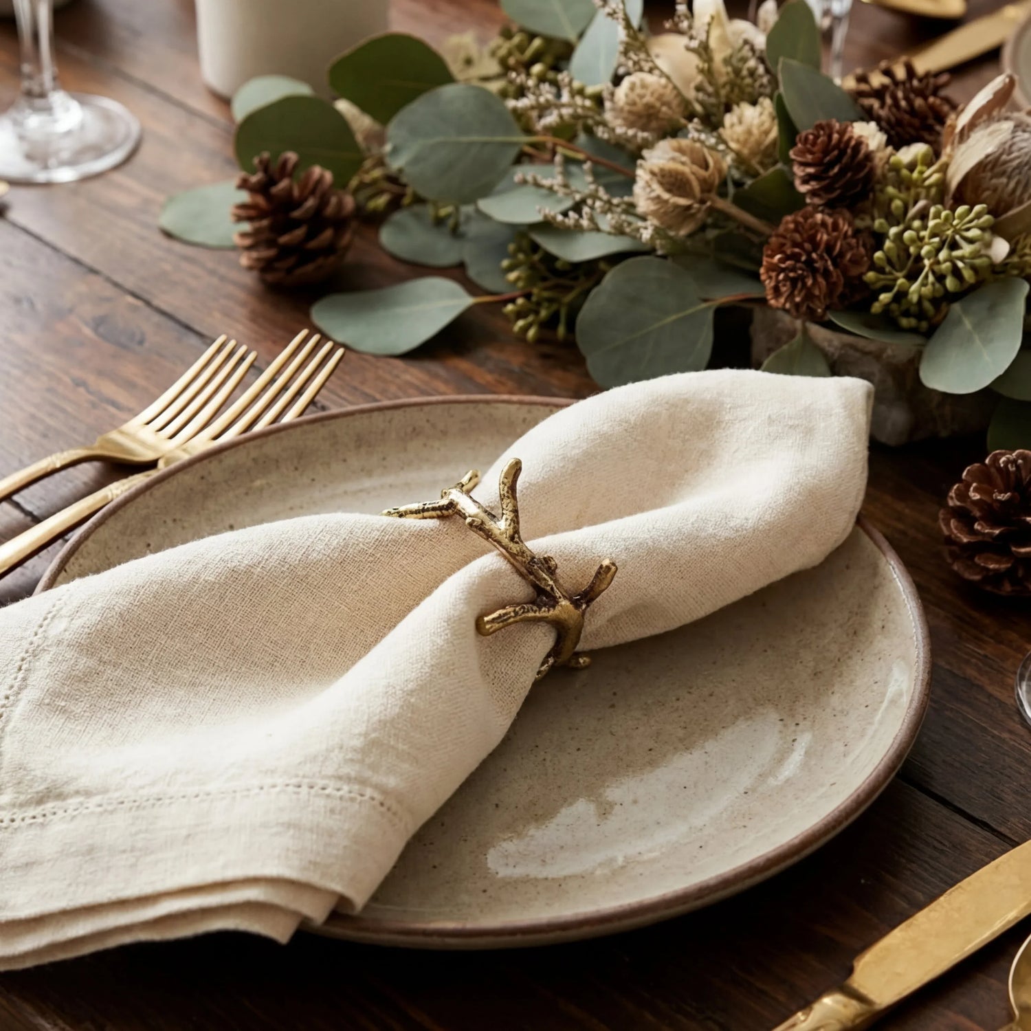 Brass Swirl Napkin Ring on a rustic table setting with speckled ceramic plate, linen napkin, and gold-plated cutlery, complemented by autumnal greenery.