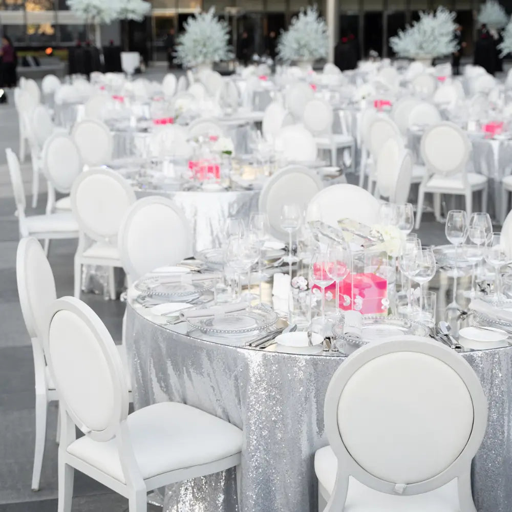 Elegant event setup featuring ROUND TABLECLOTH SEQUIN on round tables with glass chargers, floral centerpieces, and bright pink accents, ideal for formal occasions.