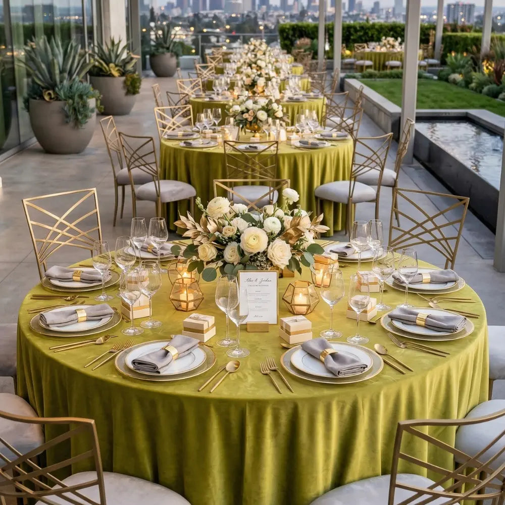 ROUND TABLECLOTH VELVET elegantly drapes a rooftop banquet table, enhancing event aesthetics with gold-rimmed settings and a floral centerpiece.