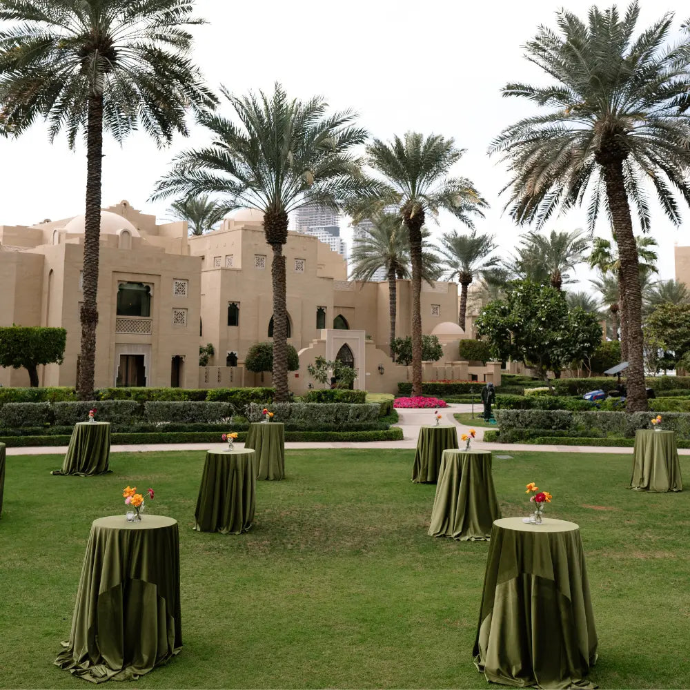 ROUND TABLE COCKTAIL setup for an elegant outdoor event, featuring olive-green linens and simple floral centerpieces, ideal for versatile party settings from Party Social.