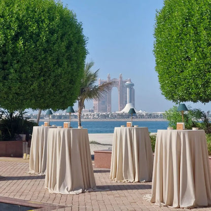 Seaside event with ROUND TABLE COCKTAIL draped in ivory tablecloths, enhancing the elegant outdoor setup with centerpieces, perfect for versatile event styling.
