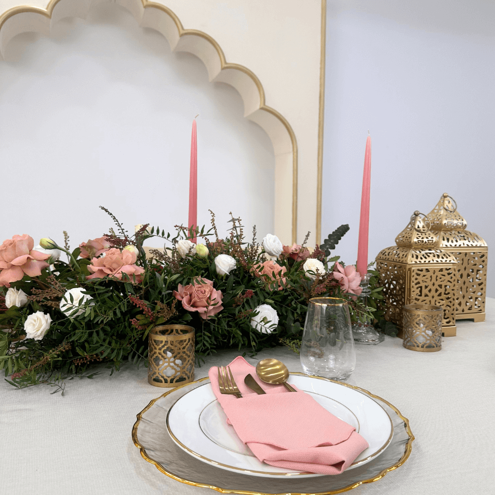 Ramadan Luxe- Dining Setup featuring a floral centerpiece, gold cutlery, glassware, candle holders, and lanterns arranged on a table for an elegant dining experience.