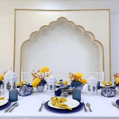 Moroccan Mirage- Dining Setup featuring a table for eight with blue and yellow plates, gold cutlery, and white Moroccan lanterns, perfect for elegant events.