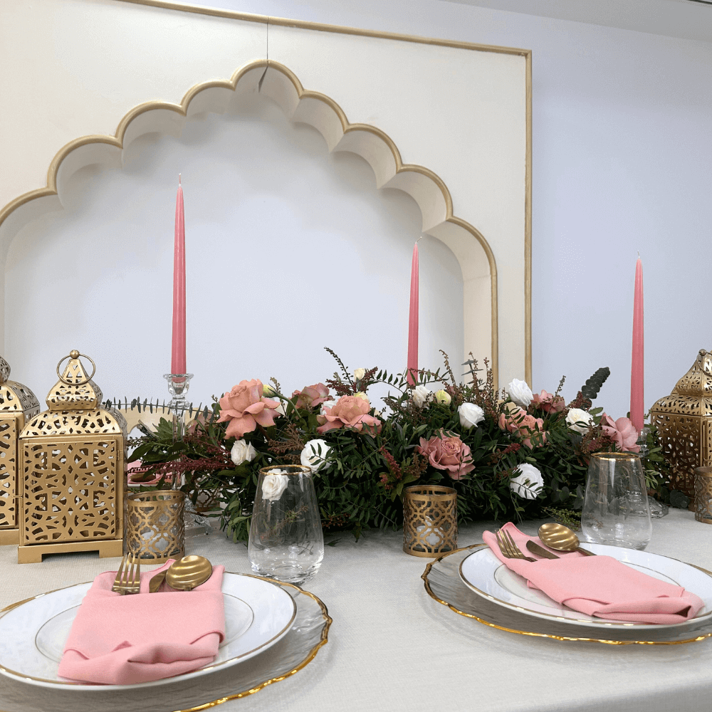 Ramadan Luxe- Dining Setup featuring a table with plates, gold cutlery, glassware, napkins, chairs, gold lanterns, candle holders, and a floral centrepiece for eight guests.