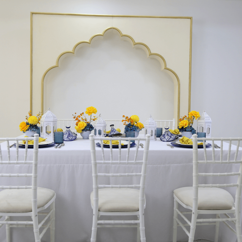 Moroccan Mirage- Dining Setup featuring a table with eight Chiavari chairs, flower centerpieces, and Moroccan lanterns, ideal for elegant dining events.