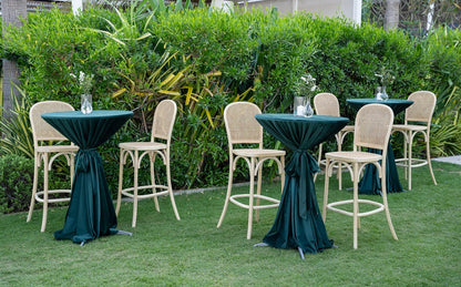 Wood Rattan Stool positioned outdoors amidst garden furniture, highlighting its vintage appeal, suitable for weddings or events.