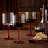 Wine glasses with red wine, a decanter, grapes, and cheese on a wooden table.