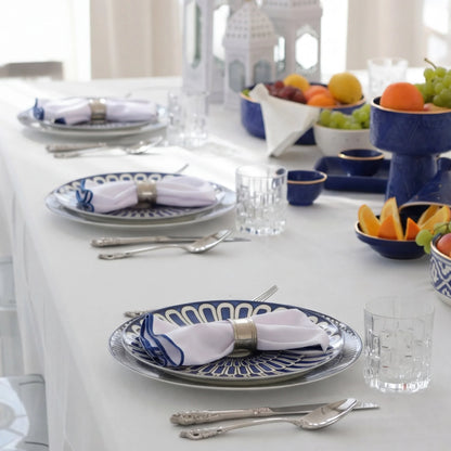 Qamar Bleu - Dinner Setup: Formal dining arrangement for 8 with patterned plates, silver napkin rings, glass tumblers, and decorative blue bowls, perfect for elegant events.