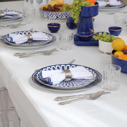 Qamar Bleu - Dinner Setup for 8 guests featuring patterned plates, gold cutlery, glass tumblers, napkins, crossback chairs, and decorative lanterns on a wooden table.