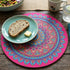 Colorful mandala placemat with a plate of bread and butter, fork, knife, and glass on a wooden table.