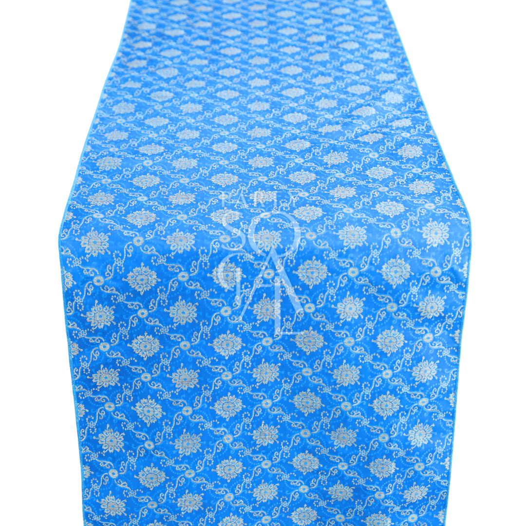 Brocade Table Runner featuring a blue tablecloth with intricate white designs, ideal for elegant tabletops at weddings and special occasions.