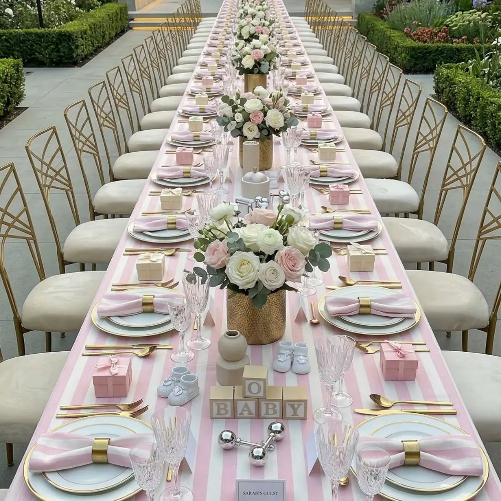 Elegant banquet table with SMALL STRIPES RECTANGULAR TABLECLOTH, gold-rimmed plates, pastel gift boxes, and baby-themed decor, set for a garden baby celebration.