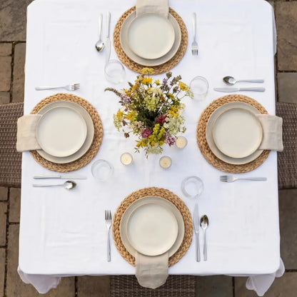 Square banquet table set with dinnerware, woven placemats, and wildflowers centerpiece, ideal for sophisticated events.