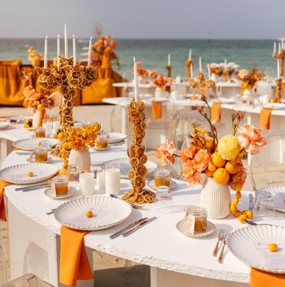 Scalloped Like Collection charger plates on a beach-side table, featuring fluted designs amidst vibrant orange elements, setting a festive, elegant tone for the event.