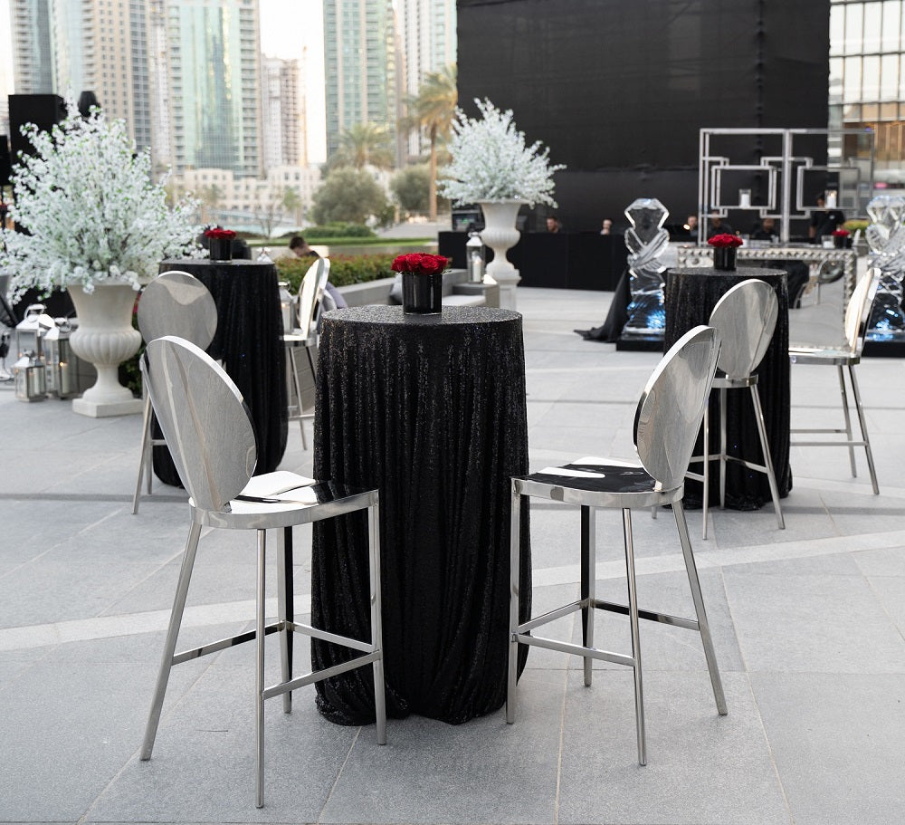 Bar stool silver with mirrored design, perfect for elevating event decor, shown alongside outdoor dining set and floral arrangements.