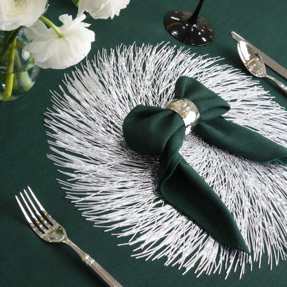 Silver Swirl Placemat on green table, featuring intricate spiral texture. Paired with a dark green napkin, silverware, and floral accents for elegant table setting.