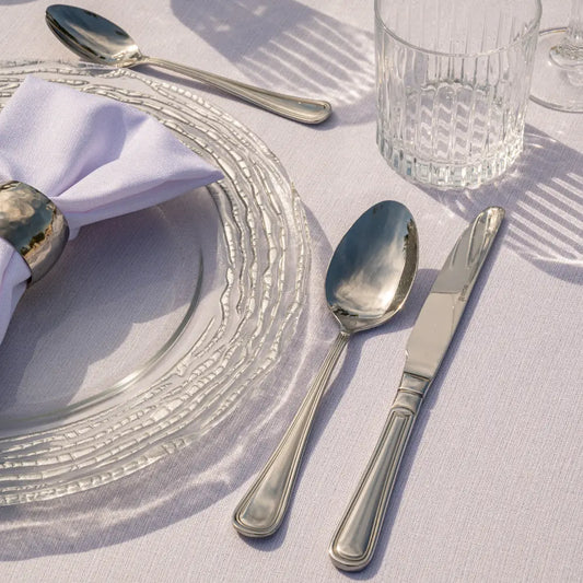 CUTLERY SIMPLE SILVER set elegantly displayed with a charger, napkin, and glass tumbler, showcasing polished stainless-steel craftsmanship ideal for formal dining settings.