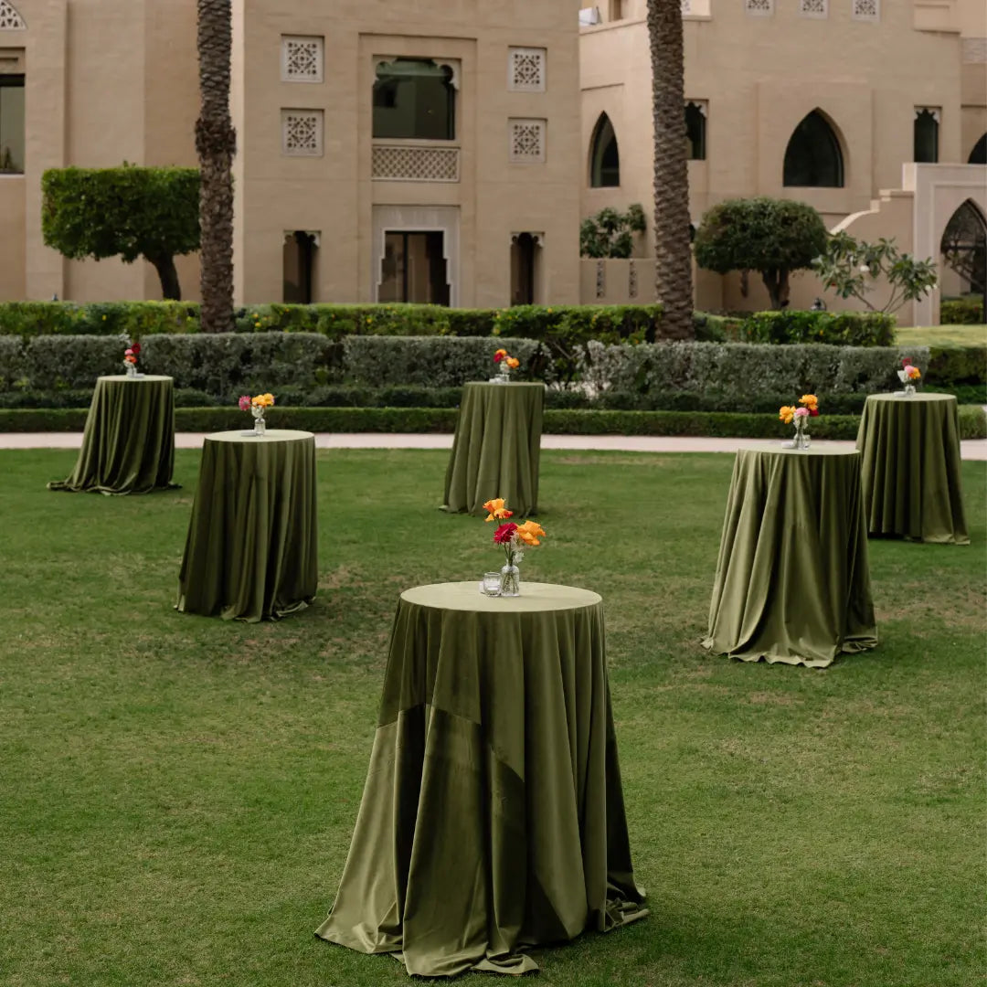 Decorative tables with green tablecloths and floral arrangements on a grassy area in front of a building.