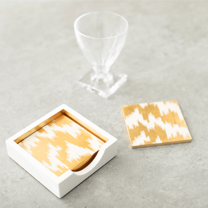 A modern Moiré square lacquer coaster set of 4 in a sleek holder, featuring glass and a white-gold box on a table. Handmade in Vietnam, showcasing art from renowned collections.