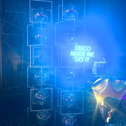 Disco Made Me Do It- LED Neon Sign positioned among disco balls, ideal for creating a lively atmosphere at parties or events.