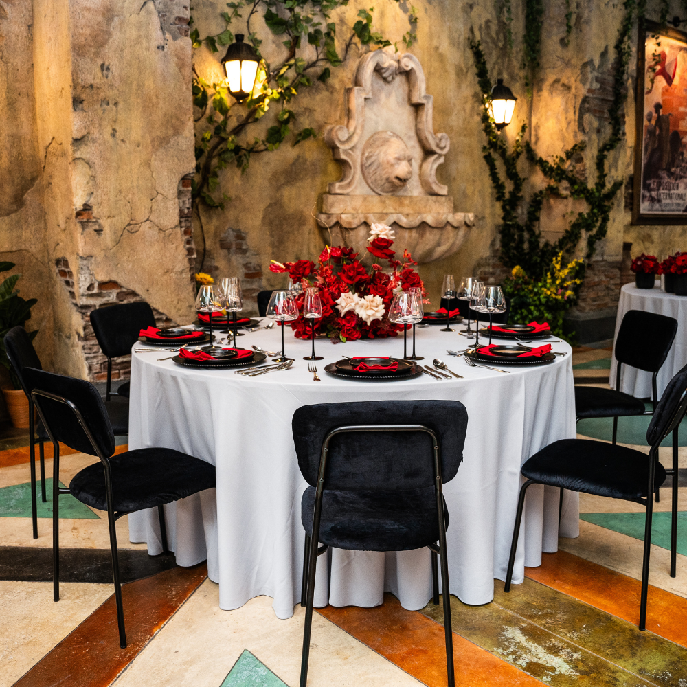 Round tablecloth in cotton linen, elegantly covering a dining table set for a dinner party, featuring a centerpiece of red and white flowers.