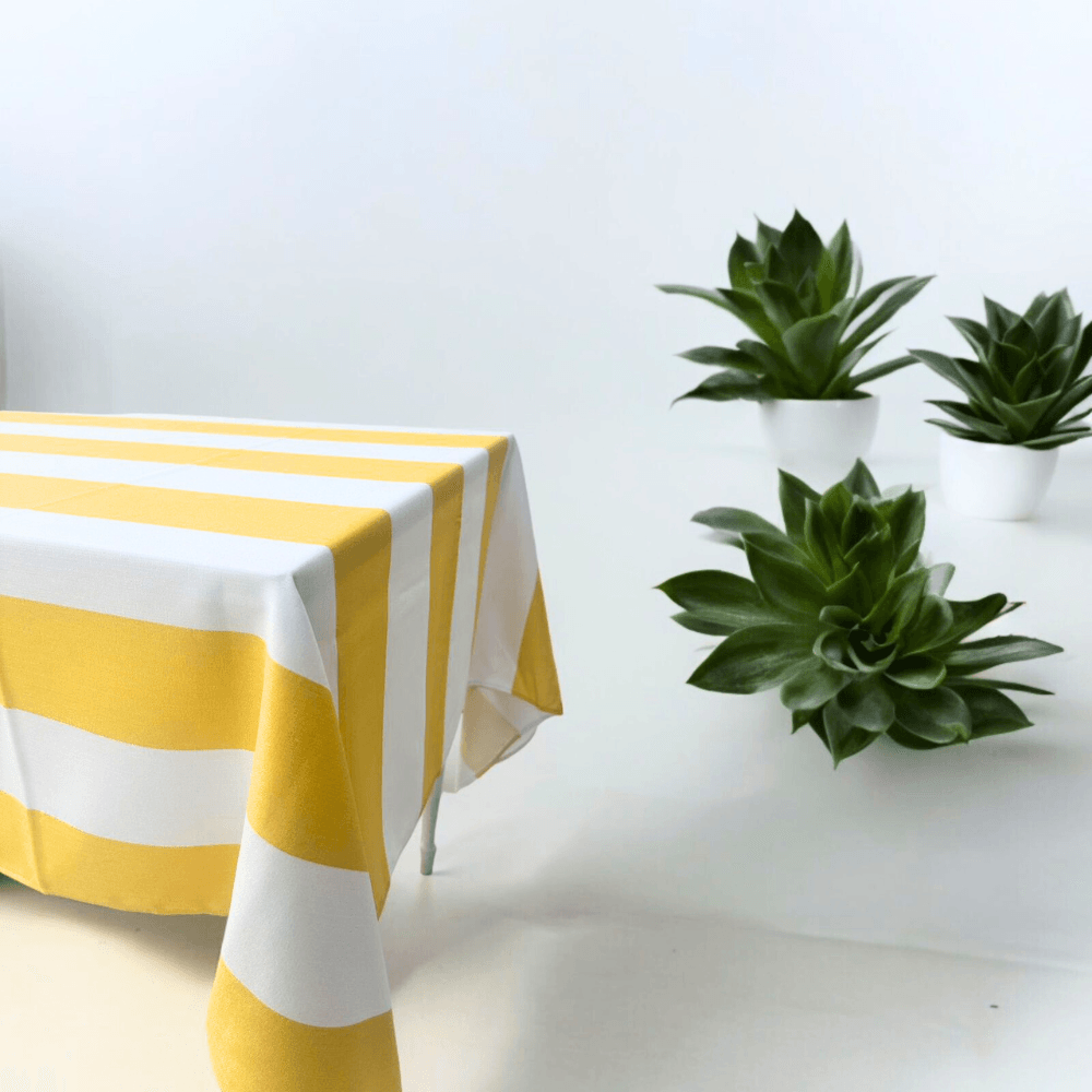 Yellow Stripe Linen Tablecloth on a table next to green plants, adding a premium touch to dinner settings; perfect for parties and events.