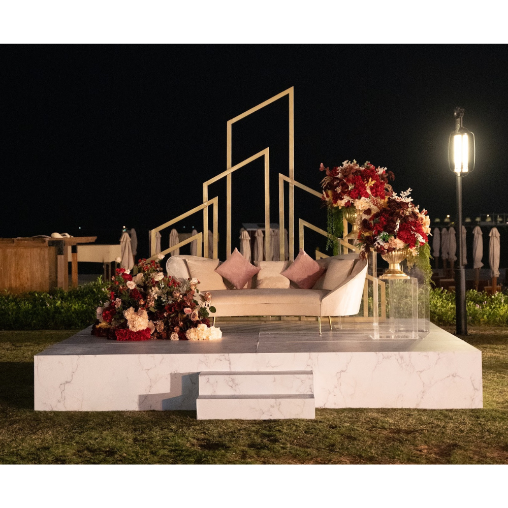 White couch with pink pillows and flowers on a marble stage, suitable for various events.