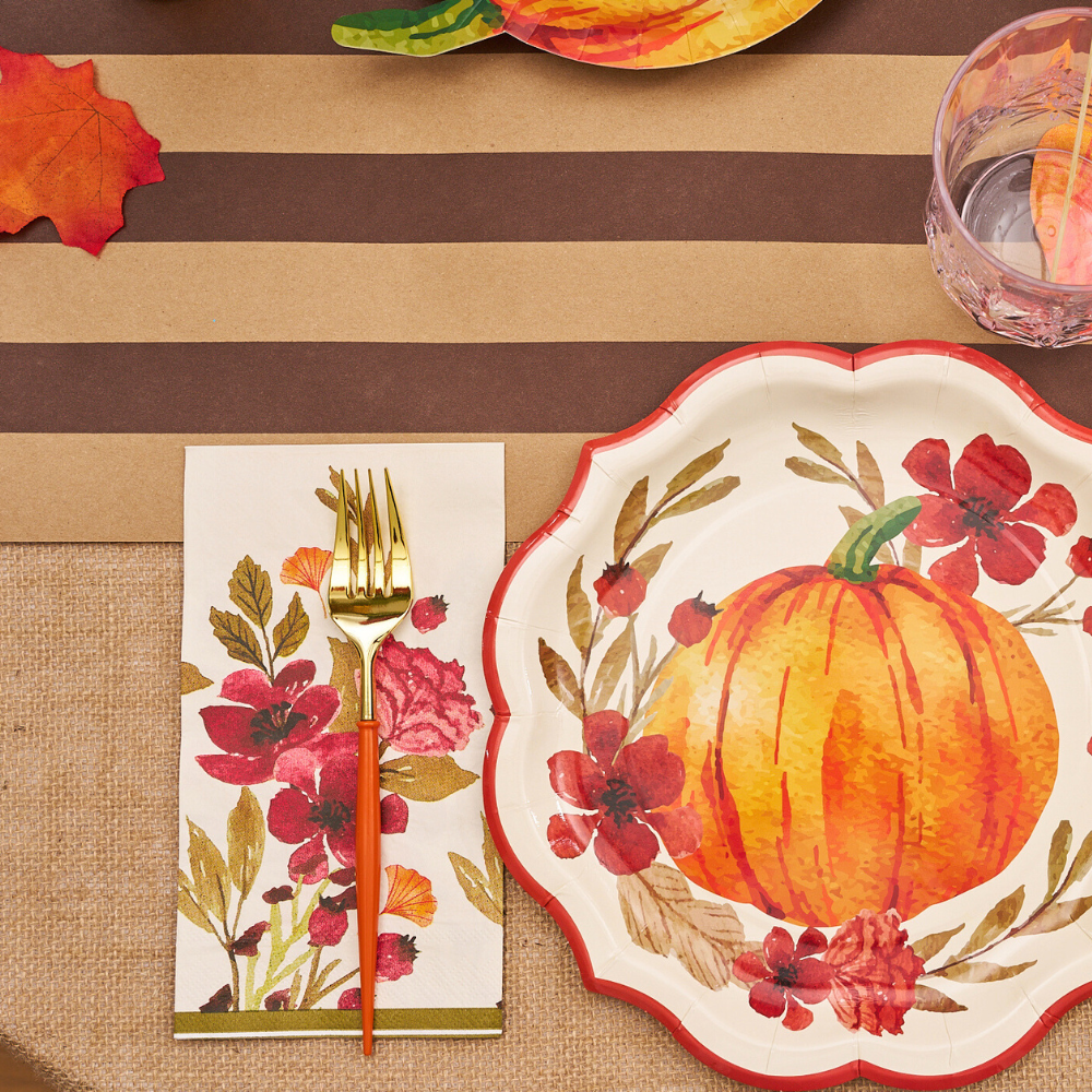 Autumn Foliage Guest Towel Napkins on a table, paired with a pumpkin-painted plate and glass, perfect for enhancing your party tablescape.