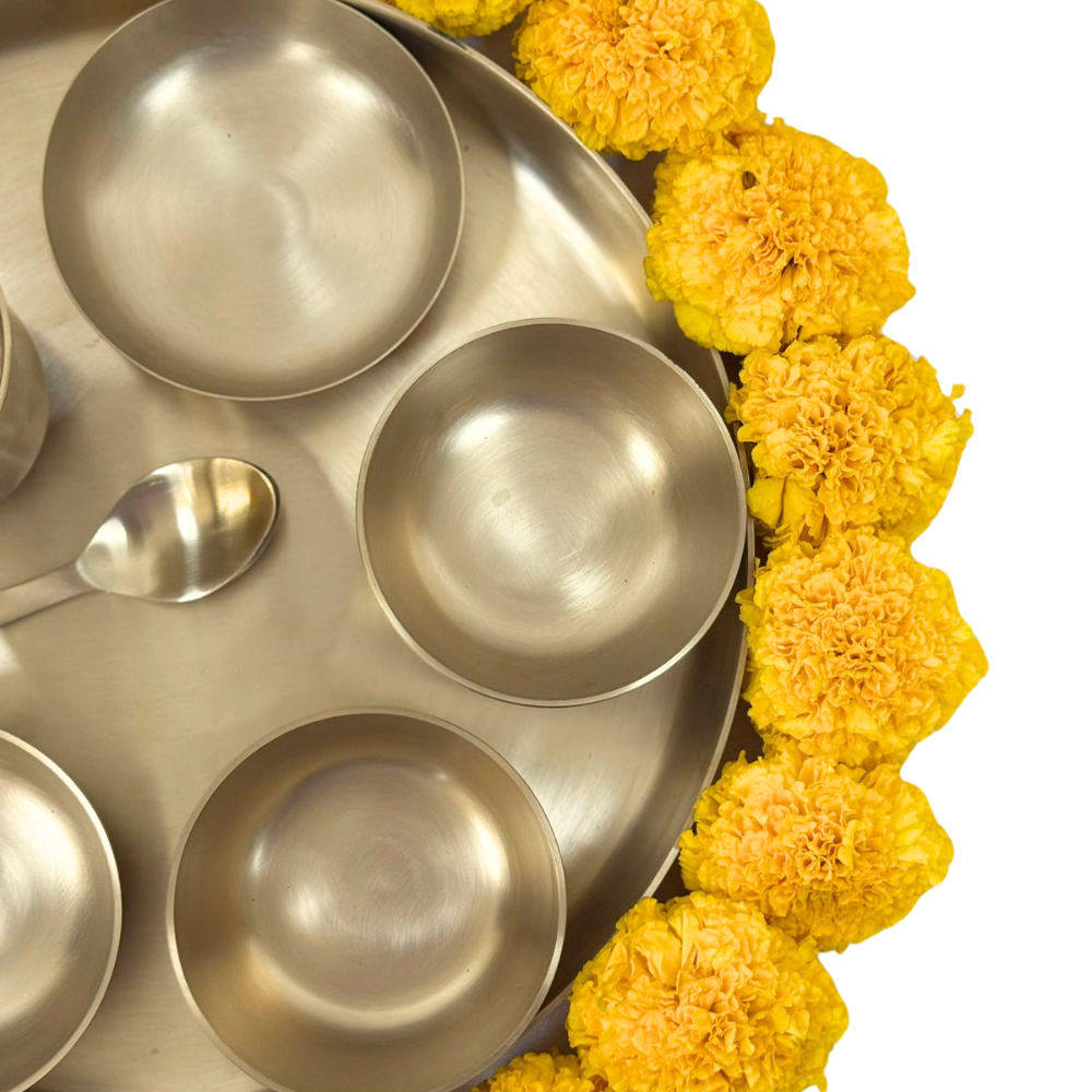 Brass Thali Set featuring bowls and spoons, accented by yellow flowers, ideal for festive gatherings. Perfect for gifts and special occasions.