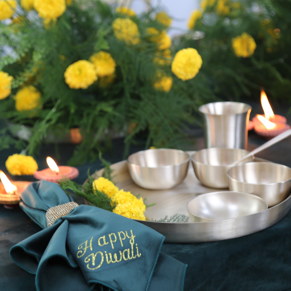 Printed Napkin (Diwali) - 4 per pack, displayed with silver tableware and vibrant flowers, enhancing festive table settings with elegant gold Happy Diwali text.