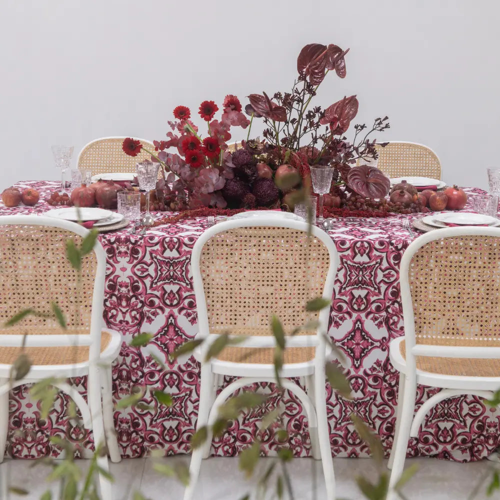 Dining table set with a floral centerpiece, patterned tablecloth, and wicker chairs.