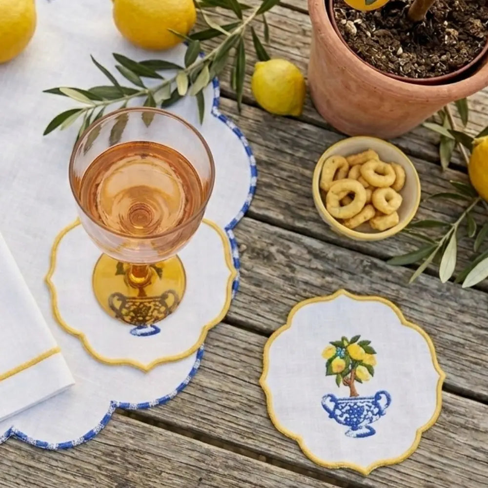 Coasters with lemon and olive design on a wooden table with a glass of wine and snacks.