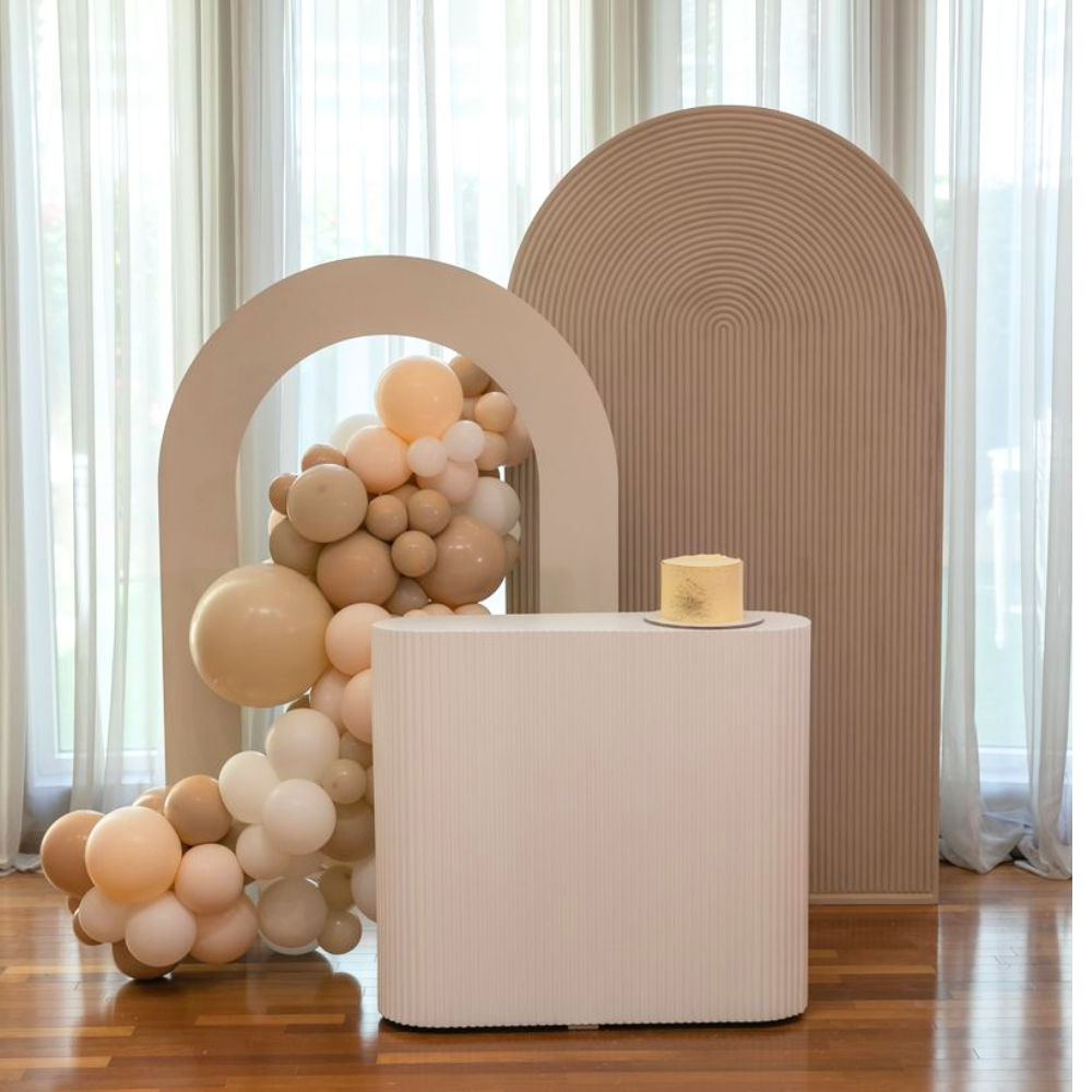 Rippled White Counter Podium on a wooden surface, surrounded by celebratory balloons, ideal for enhancing event settings like weddings or birthdays.