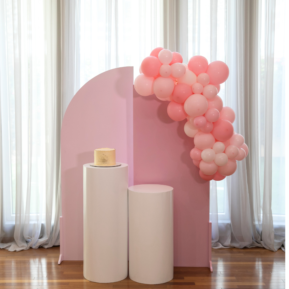 Pink Elegance Backdrop featuring pink and white display with balloons and a cake on a pedestal, perfect for enhancing party decor.