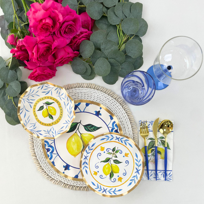 Capri Coast Paper Salad &amp; Dessert Plate- 8 Per Package: Elegant plates with blue pattern, lemons on white background. Perfect for events. Image: Table with plates, flowers, blue liquid, gold utensils. Store: Party Social - Your go-to for party essentials.