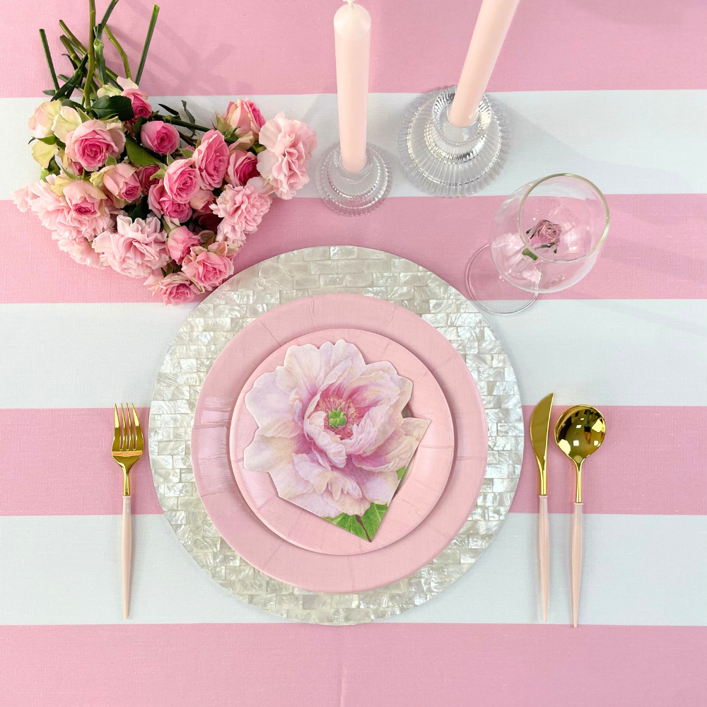 A chic Round Shell Placemat, 1 each, on a table with pink and white striped tablecloth, paired with pink plates and flowers. Ideal for stylish table setups.