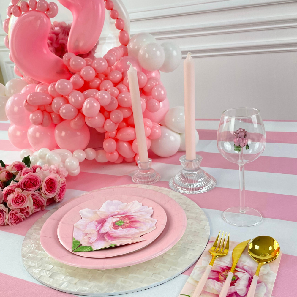 A Clear W/ Rose Charm Glass amidst a table set with pink plates, balloons, and a pink balloon sculpture. Ideal for events, adding a colorful touch to any themed party.