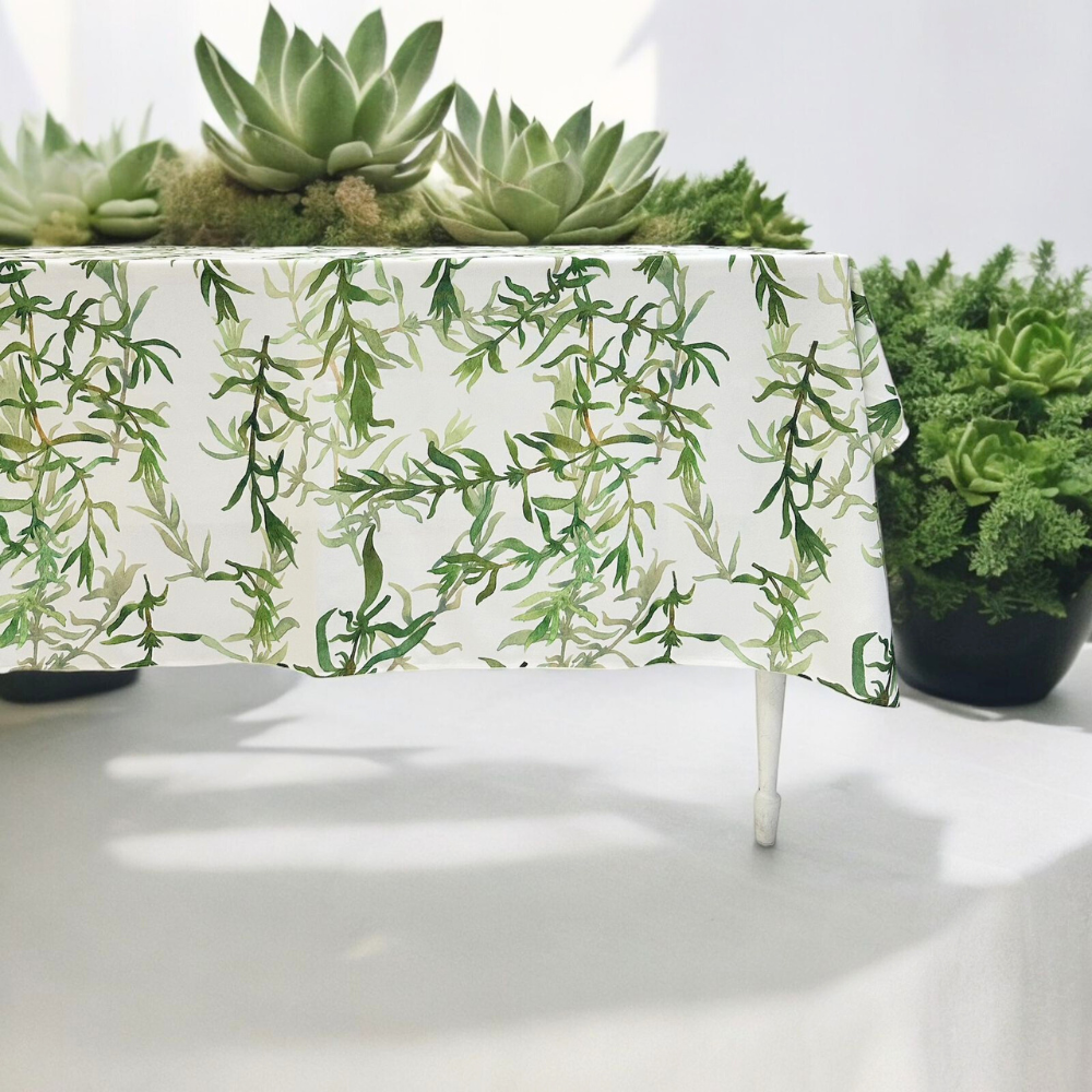 Gardenia Linen Tablecloth featuring a white tablecloth with green leaf prints, elegantly styled on a table with decorative plants.