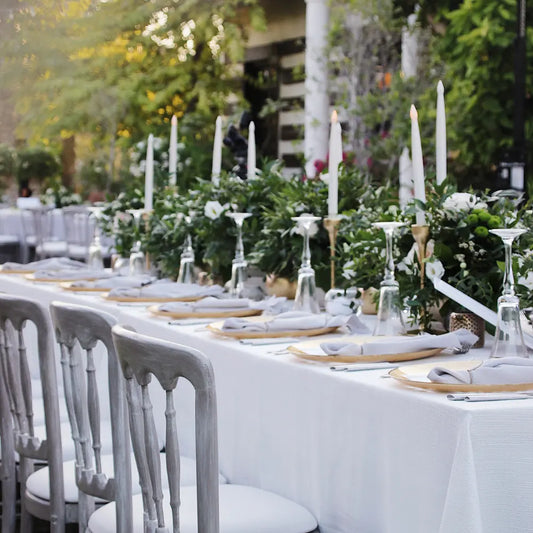 Rectangular Tablecloth Linen Blend elegantly drapes a long dining table, set with greenery, candles, and place settings for an outdoor event.